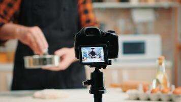 Close up of a video camera filming senior smiling man blogger in kitchen cooking. Retired blogger chef influencer using internet technology communicating on social media with digital equipment photo