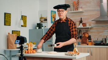 Cheerful elderly man recording the recipe step by step in hoe kitchen. Retired blogger chef influencer using internet technology communicating, shooting blogging on social media with digital equipment photo