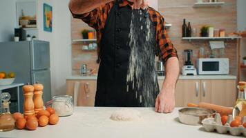 Bakery man sifting wheat flour, preparing bread dough. Retired elderly chef with bonete and uniform sprinkling, sieving spreading rew ingredients with hand baking homemade pizza and bread. photo