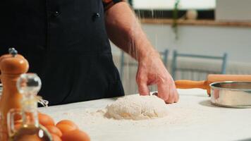 Baker adding flour on the pile by hand preparing bread dough. Close up of retired elderly chef with bonete and uniform sprinkling, sieving spreading rew ingredients baking homemade pizza and cackes. photo