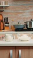 Pastry ingredients for homemade cakes and bread in empty kitchen. Modern dining room equipped with utensils ready for cooking with wheat flour in glass bowl and fresh eggs on table photo