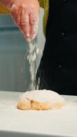 abuela preparando hecho en casa rosquillas vistiendo cocina delantal. retirado mayor cocinero con bonete y uniforme aspersión, tamizado cernido trigo harina con mano horneando hecho en casa Pizza y un pan. foto