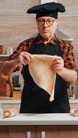 Chef cooking handmade pasta with healthy ingredients at home in modern kitchen. Happy elderly baker with bonete using wooden rolling pin, sprinkling, sieving flour on table, baking traditional cookies photo