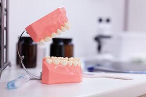 Teeth jaw standing on table in orthodontic dentistry hospital room while doctor explaining stomatology diagnosis. Model of plastic tooth accessory using for oral dental healthcare hygiene photo