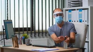 Freelancer wearing protection face mask cleaning hands with sanitizer gel at workplace. Entrepreneur working in new normal office disinfecting using antibacterial alcohol against corona virus. photo