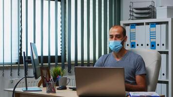 Man using laptop discussing project online wearing protective mask. Freelancer working in new normal office workplace chatting talking having virtual conference, meeting, using internet technology photo