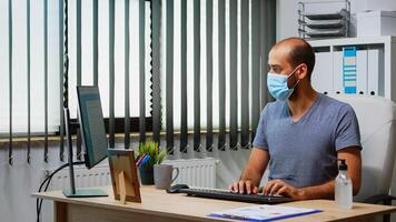 Employee with mask cleaning hands with antibacterian gel in office room before working at computer. Entrepreneur working in new normal office workplace using sanitize alcohol gel against corona virus photo