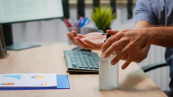 Close up of man using antibacterian gel before writing on computer. Entrepreneur working in new normal company office workplace cleaning disinfecting hands using sanitize alcohol against corona virus. photo