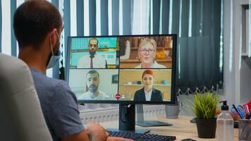 espalda ver de hombre con máscara hablando en vídeo llamada con remotamente colegas. persona de libre dedicación trabajando en nuevo normal oficina lugar de trabajo chateando durante virtual conferencia, reunión, utilizando Internet tecnología foto