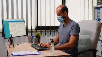 Worker wearing protection mask using sanitiser gel during coronavirus. Entrepreneur working in new normal office workplace in company cleaning hands using antibacterian alcohol against corona virus. photo