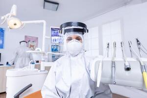 Patient pov of dentist explaining teeth treatment dressed up in covid protective suit. Stomatolog wearing safety gear against coronavirus during heatlhcare check of patient. photo