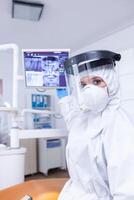 Patient pov in dental office looking at doctor showing digital teeth x-ray on monitor. Stomatology specialist wearing protective suit against infection with coronavirus pointing at radiography. photo