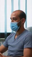 Man with protective mask during video meeting sitting alone in office. Freelancer working in new normal workplace chatting talking having virtual conference, webinar, using internet technology photo