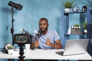 Smiling blogger using camera for recording video and creating digital content for online blog. African american vlogger talking in mic while broadcasting on videoblog channel photo