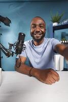 Smiling african american blogger speaking in microphone and holding camera portrait. Cheerful streamer talking with subscribers while recording video for internet channel photo