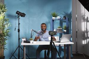 African american blogger using camera for web streaming in professional studio. Smiling young man vlogger creating digital content and recording video with videography equipment photo