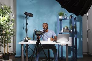 Smiling vlogger recording video and looking at professional camera while working in studio. Cheerful african american blogger filming digital content with videography equipment photo