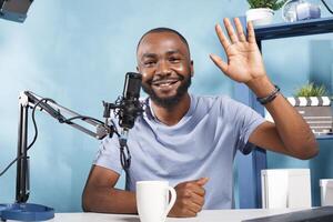 Cheerful vlogger streaming online and greeting subscribers portrait. Smiling african american man blogger recording video, creating digital content and waving hello portrait photo