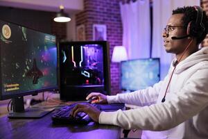 Gamer playing classic arcade space videogame, doing flying maneuvres through asteroid clusters. African american man using high tech gaming computer to solve levels in singleplayer game photo