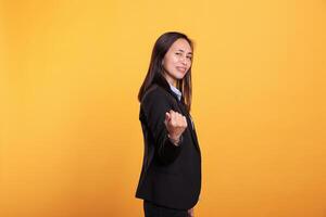 Smiling filipino businesswoman gesturing come to me, beckoning with finger posing in studio over yellow background. Cheerful woman inviting you for confidential talk. Calling symbol photo