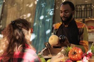 Young local seller showing organic healthy products from farmers market stall, locally grown food. Male farmer talking to customer about various seasonal fresh veggie produce. photo