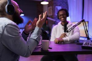 Online show host recording podcast with guest, telling jokes to eachother in home studio living room. Happy men having fun together during broadcasting session for internet streaming service photo