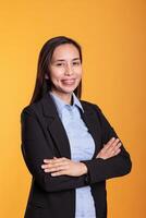 Positive brunette woman standing in arm crossed posing over yellow background, smiling at camera during studio shoot. Smiling filipino adult with cheerful expression enjoying break time photo
