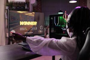 Cheerful gamer celebrating winning online multiplayer spaceship videogame tourney, defeating enemies. Woman enjoying leisure time in brick wall apartment, feeling good about victory photo