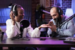 Cohosts presenting religion podcast in professional studio, teaching prayers to audiences. Presenter using high quality recording setup to film spirituality conversation, doing hands together gesture photo