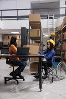 Asian postal service worker in wheelchair and operator maintaining parcel delivery. Storehouse order packer with disability giving cardboard box to distribution manager in storage room photo