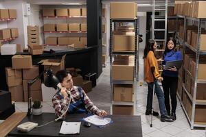 Delivery operators managing warehouse product audit in storage room. Retail industry storehouse employees working together, tracking parcel transportation online on laptop photo