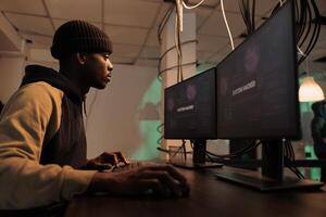 African american thief working with encryption to hack computer system, hacking network to steal database information. Male spy breaking into government server, planting trojan virus. photo