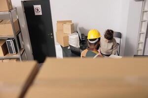 Diverse warehouse employees planning merchandise inventory, analyzing products checklist in storage room. Stockroom supervisor discussing clients orders with worker before start preparing packages photo