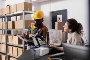 African american coworker analyzing goods checklist with stockroom manager, discussing merchandise inventory l in warehouse. Diverse team working at clients online orders in storage room photo