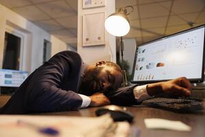 agotado cansado ejecutivo gerente sufrimiento desde somnolencia después trabajando tarde a noche en puesta en marcha oficina. agotado africano americano trabajador con agotamiento síndrome dormido a trabajar. negocio concepto foto