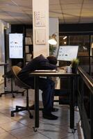 Exhausted manager with burnout syndrome resting at work, after working overtime at company investment report. Tired african american entrepreneur sleeping on desk in startup office photo