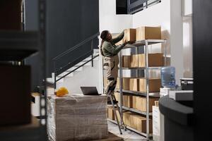 Storehouse employee taking out carton boxes from shelf, preparing customers orders in storage room. African american stockroom supervisor working at shipping details for packages in warehouse photo