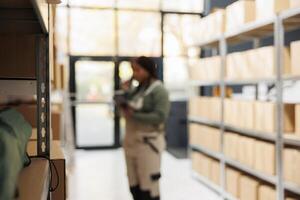 Selective focus of shelves full with boxes ready for delivery, in background stockroom manager talking at landline phone with remote supervisor. African american employee preparing customers orders photo