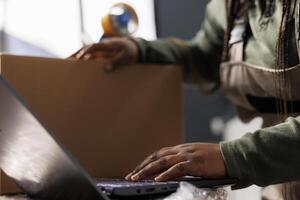 cerca arriba de almacén empleado analizando bienes logística en ordenador portátil computadora, trabajando a mercancías calidad controlar reporte en almacenamiento habitación. africano americano supervisor preparando clientes pedidos foto