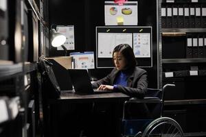 profesional mujer de negocios contabilidad empleado en silla de ruedas escritura presupuesto plan y contabilidad estrategia en ordenador portátil. asiático mujer en repositorio lleno con documento carpetas y diagramas de flujo foto