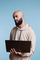 Puzzled arab man programming on laptop and looking away with confused expression. Confused person in doubt while developing software app and writing code on portable computer photo