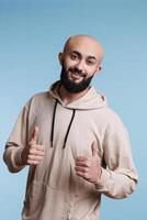 Cheerful arab man showing approval gesture with two thumbs up portrait. Smiling person with joyful facial expression standing with satisfaction sign while looking at camera photo