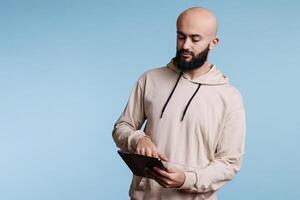 Arab man using digital tablet, surfing internet and tapping on touchscreen. Young focused person holding portable gadget, browsing social media networks and scrolling online pages photo