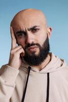 Arab man grimacing in pain while having migraine and holding head with finger portrait. Young bearded person rubbing temples while suffering from headache and looking at camera photo