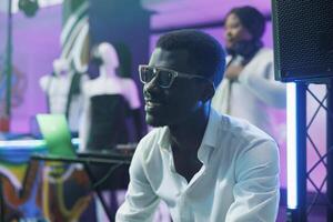 Smiling carefree african american man in sunglasses relaxing in nightclub. Young cheerful clubber sitting in club while attending live music discotheque and enjoying nightlife leisure entertainment photo