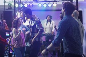 Young people dancing and partying at social gathering in nightclub with spotlights. Energetic clubbers relaxing on crowded dancefloor while clubbing at live music concert festival photo