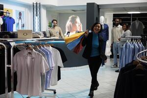 ropa Tienda satisfecho cliente caminando con compras pantalones en ropa Tienda y mirando a cámara. alegre sonriente asiático mujer que lleva papel pantalones con de moda vestir compra en centro comercial foto