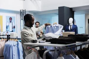 African american man checking shirt while exploring apparel rack in clothing store. Fashion boutique customer searching for formal garment while shopping in menswear section photo