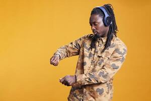 African american man dancing and vibing on favourite music in studio over yellow background, enjoying free time. Joyful adult wearing headset, having fun with dance while showing funny moves photo