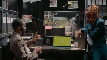 equipo de ley agentes mirando a pantalla verde en computadora portátil, analizando delincuente registros en policía archivo archivos. privado detectives examinando aislado Bosquejo modelo con blanco croma llave. foto